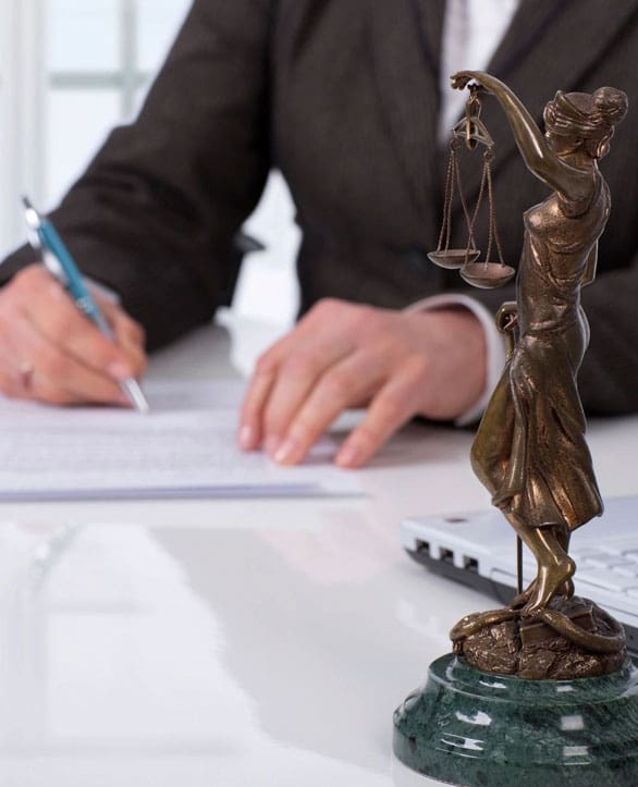 A person writing on paper next to a statue of lady justice.