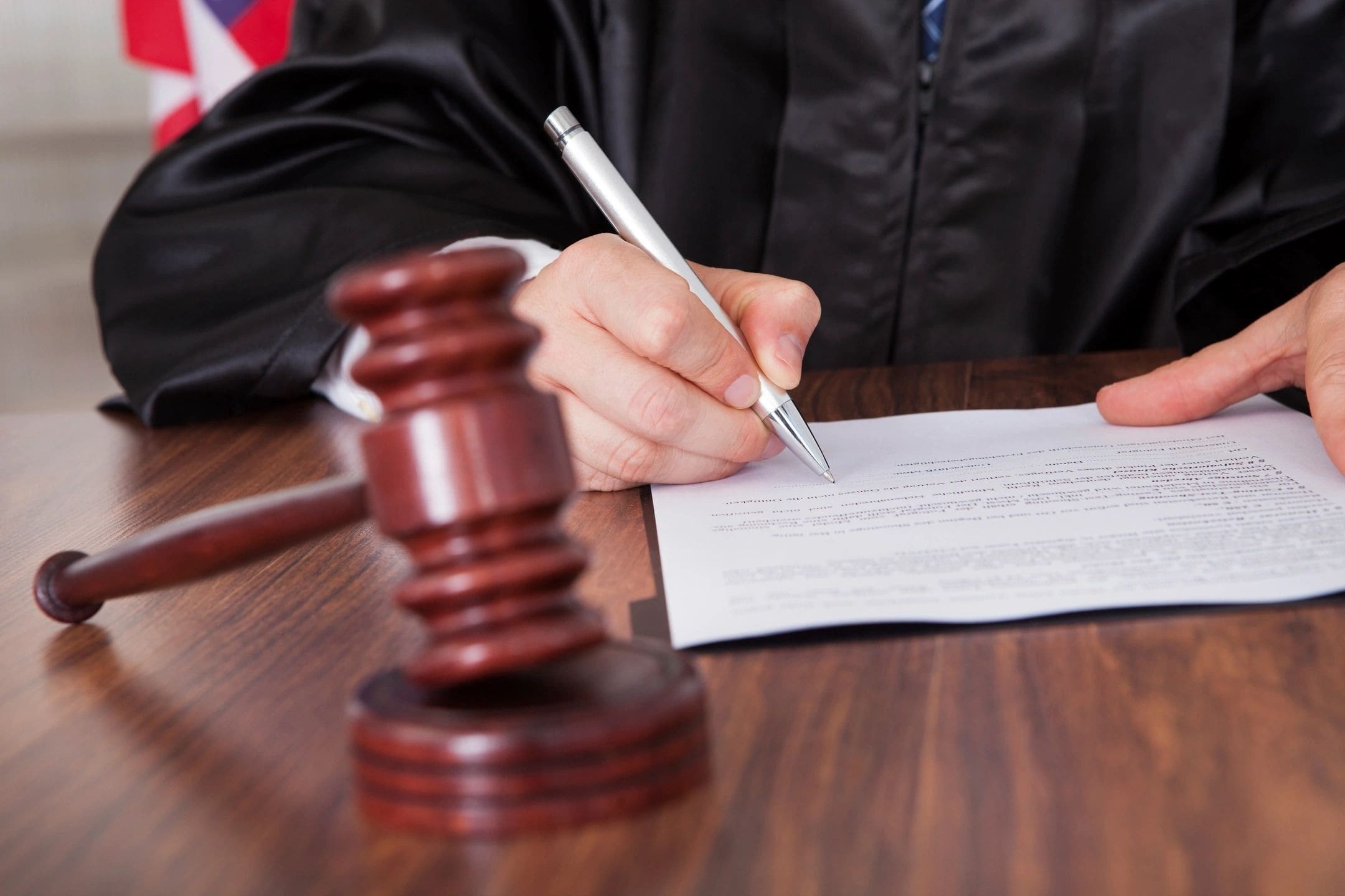 A judge writing on paper next to a gavel.