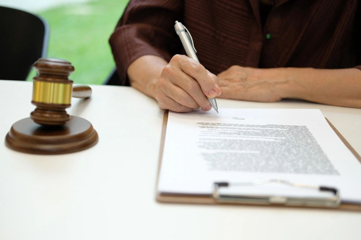 A person writing on top of papers next to a judge 's gavel.