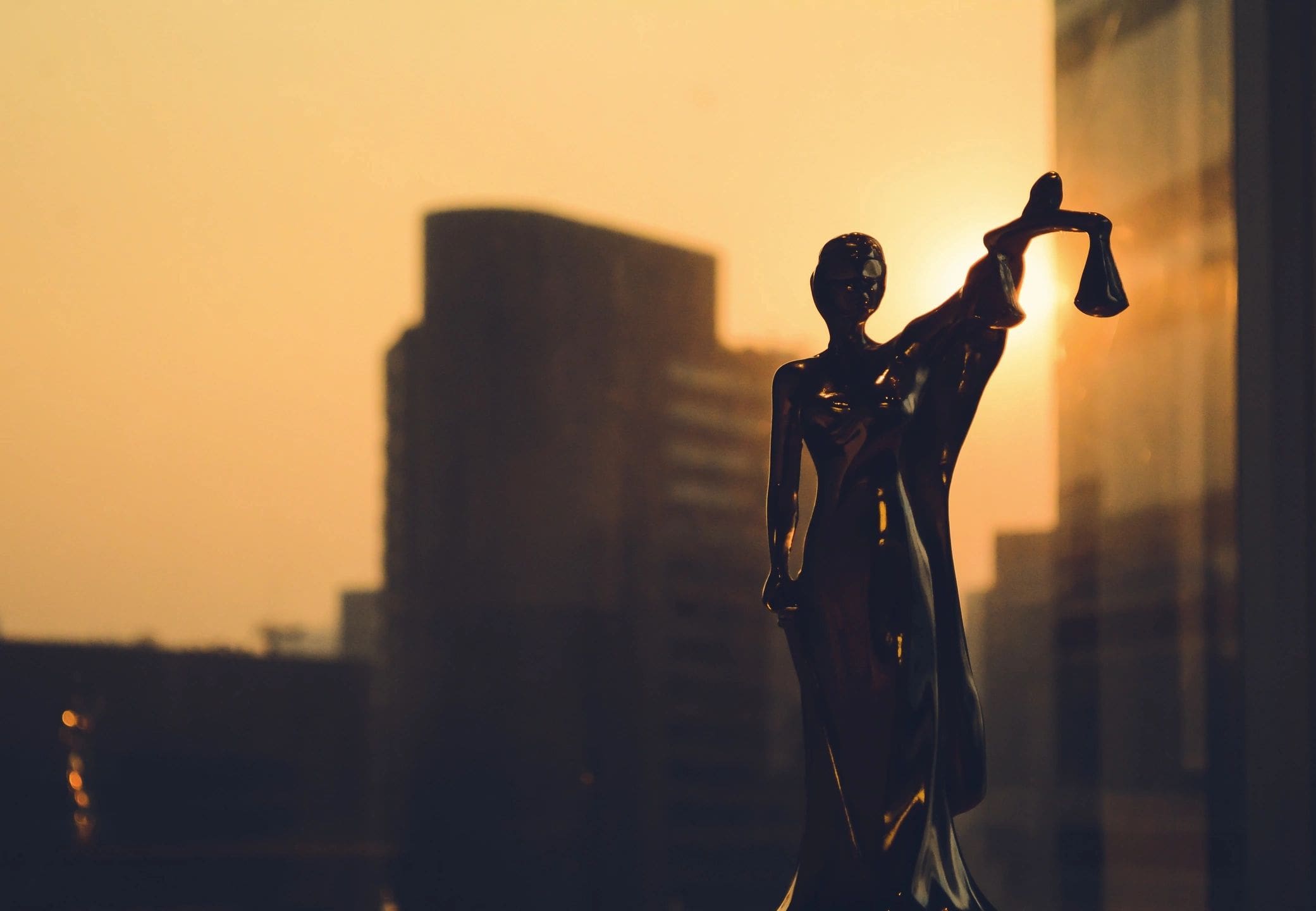 A statue of lady justice in front of the sun.